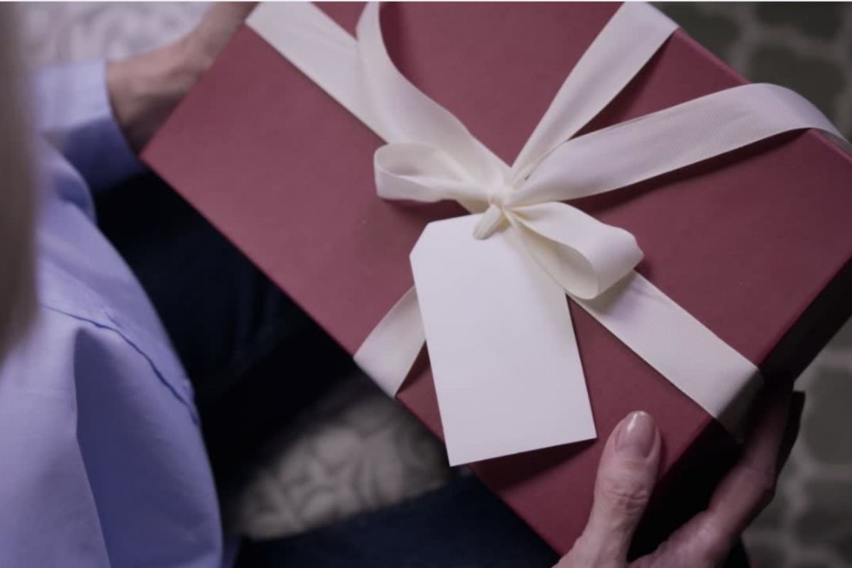 Osoba drzi elegantnu poklon kutiju sa belom masnom i praznim tagom za poruku